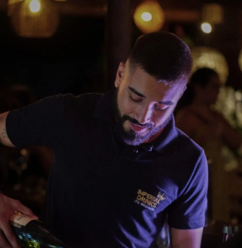 Diego Bandeira servindo espumante em uma taça, com camisa bordada da Imperial Drink’s.