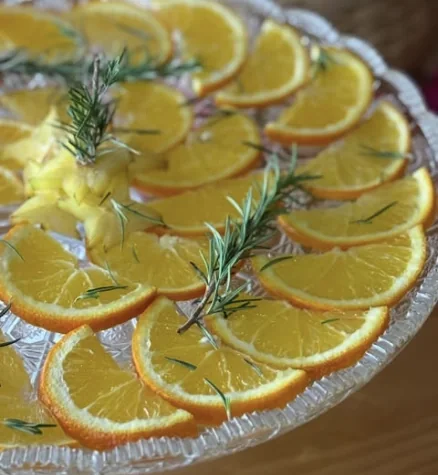 Rodelas de laranja com ramos de alecrim em travessa de vidro lapidado.