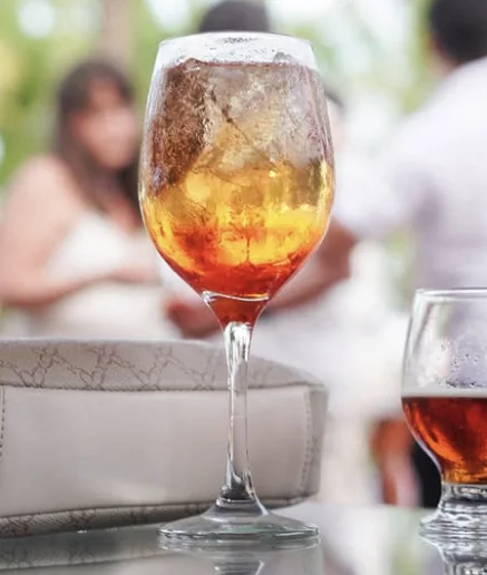 Drink âmbar com gelo em taça, servido durante uma festa de casamento.
